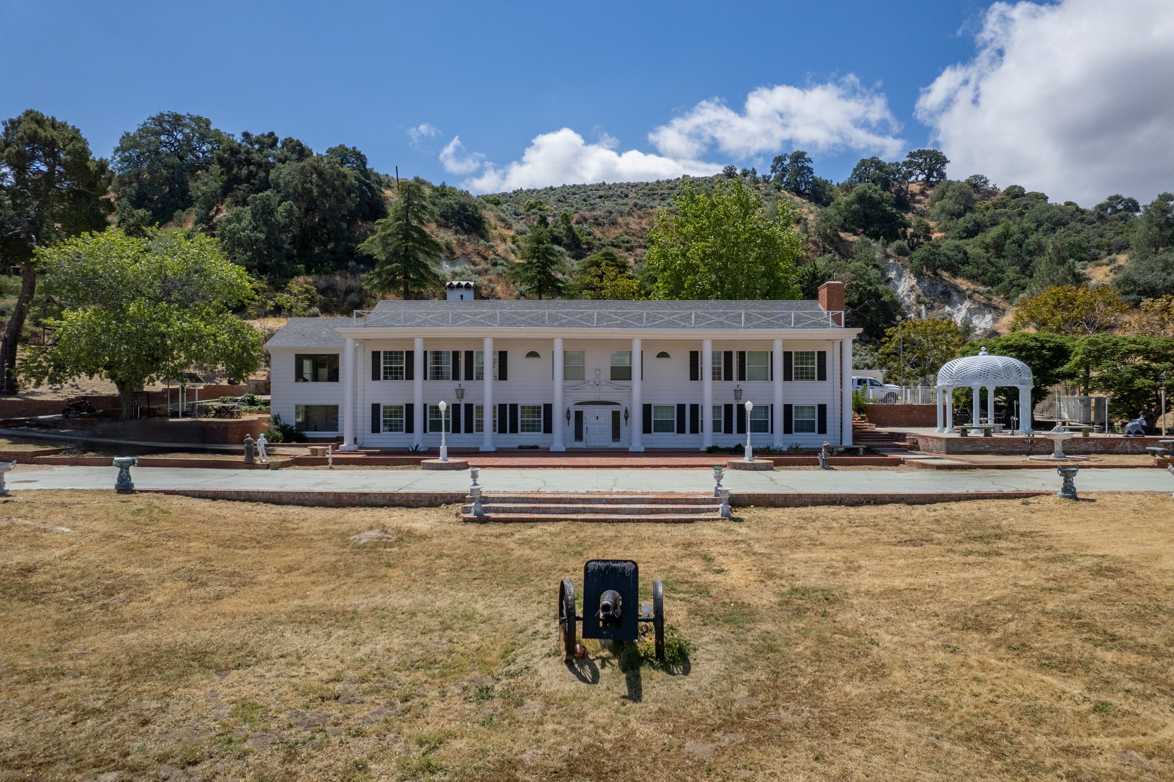 White colonial estate with a gazebo, set against oak-covered hills